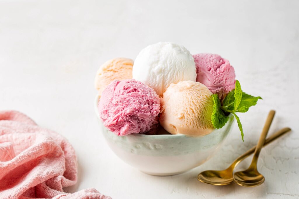 Assorted fruit and berries ice cream in a bowl, lemon, strawberry and peach flavors scoop, balls with fresh mint. White background.